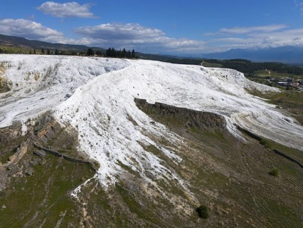 White limestone hills in a natural setting under a blue sky with clouds, aerial view, sinter