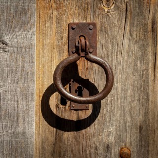 A weathered wooden door showcases an ornate metal knocker and an antique keyhole, reflecting the