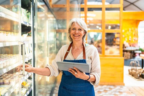 Smiling senior supermarket employee taking notes on a digital tablet while checking products in a