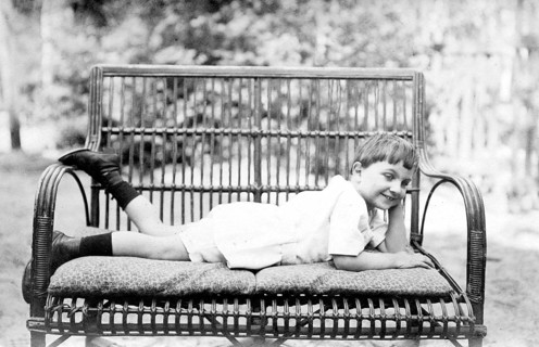 Young boy lying on a bench outdoors, 1920s, A boy lies smiling on a comfortable couch in the