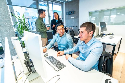 Two customer service representatives working on computer in a busy call center, assisted by their