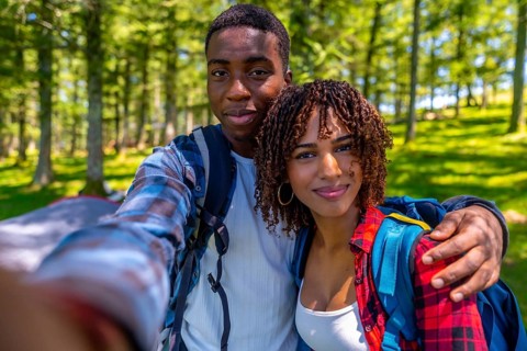 Young hikers with backpacks enjoying a sunny summer day, capturing a joyful selfie portrait amidst
