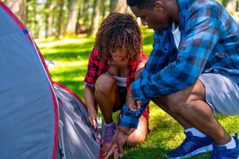 Young couple setting up a camping tent on a grassy campsite in a serene forest, embracing the joys
