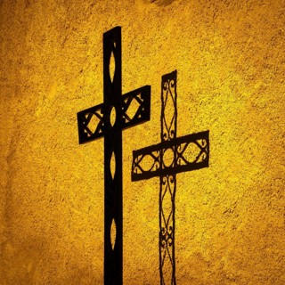 Shadow cast by one ornate cross on a textured wall at sunset illuminates the religious significance