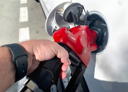 Male hand holding gas pump nozzle pumping gas into vehicle