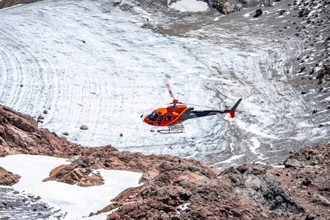 Red helicopter flies over glaciers in the mountains, Stubai Alps, South Tyrol, Italy