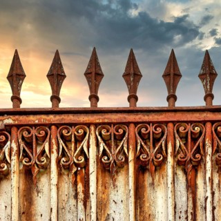A rusty ornate gate stands tall, featuring intricate designs and pointed spikes. The backdrop shows