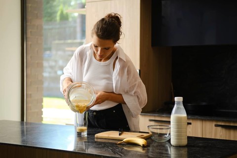 A person blends banana and sea buckthorn in a cozy kitchen. Ingredients are prepared on the