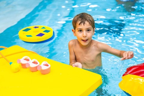 Happy boy enjoying playful moments with colorful floating toys in a swimming pool, embracing the