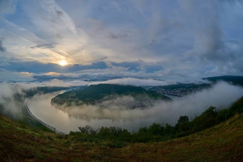 River landscape in a bend with misty hills and cloudy sky illuminated by the sunrise, summer, Rhine
