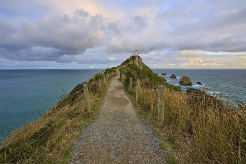 A path leads to a lighthouse on a rocky cliff by the sea, summer, Nugget Point Lighthouse, Ahuriri