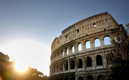 The Colosseum stands majestically against a setting sun, highlighting its ancient stone structure