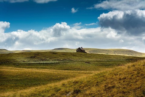Ruined stone cottage stands alone on a grassy hillside under a partly cloudy sky in a remote