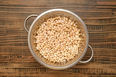 Dried white beans being rinsed in a metal colander on a wooden kitchen countertop