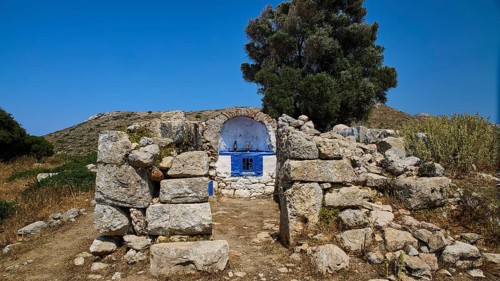 Stone chapel with blue façade amidst ancient ruins, embedded in lush vegetation, Artemis Temple,