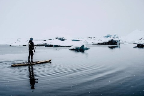 Man stand up paddling, snowfall, glacial lake Jökulsarlon at Vatnajökull, Iceland* Man stand up