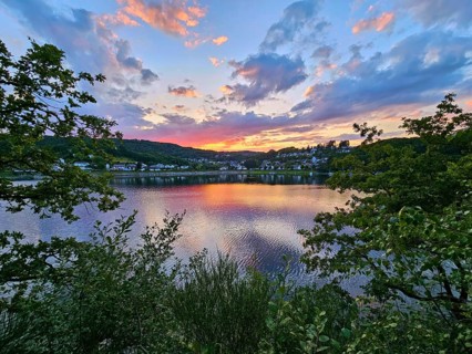 Colourful sunset over a calm lake, surrounded by trees and reflecting clouds in the sky, summer,
