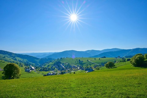 Sunny panoramic view of a village surrounded by green hills under a clear sky, spring,
