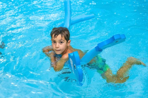 Young boy enjoying summer days, playing with a blue floating toy in a refreshing blue pool under