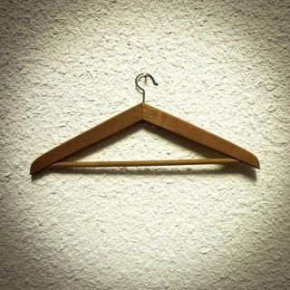 A wooden clothes hanger is resting on a textured wall, showcasing its natural finish and design.
