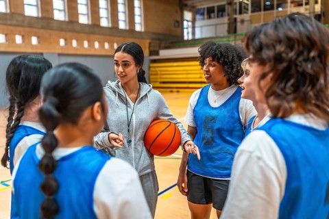Female basketball coach holding ball and explaining game strategy to her team during training in a