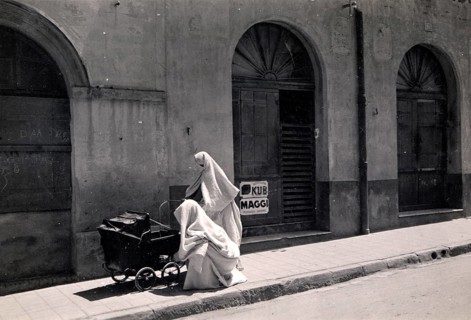 Two Arab women with prams, 1910s, A veiled person sits next to a pram in front of an old building