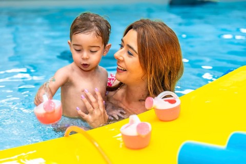 Mother and baby daughter enjoying playful moments with colorful toys in a swimming pool, creating