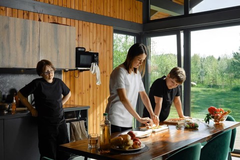 Mother skillfully prepares healthy food on a wooden table while two children watching. Natural