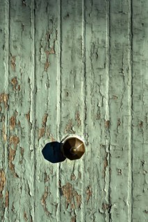 The image captures a close-up of a rustic doorknob on an old, weathered wooden door. The green