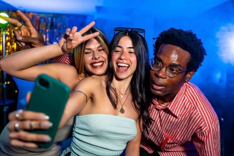 Happy multi ethnic friends taking a selfie while partying in a nightclub, making peace signs and