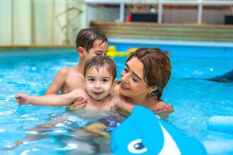 Mother and two sons enjoying time together, playing with inflatable toy in home swimming pool,