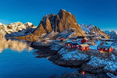 Fishermen's Village in front of snowy mountain range at the coastline in winter, Lofoten, Norway