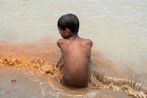 A boy sits in the bank of Brahmaputra River as he bathe to seek relief from the intense summer heat