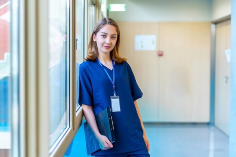 Confident young doctor wearing blue scrubs holding a clipboard while standing in a modern hospital