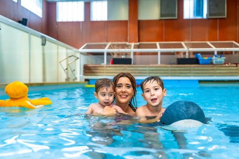 Mother and children enjoying playful moments, laughing and splashing together in the swimming pool