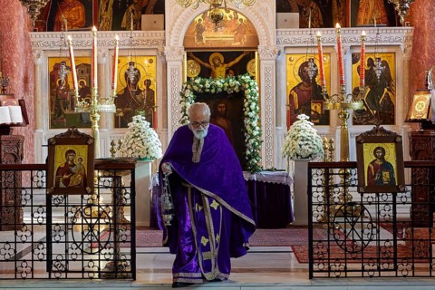 Priest in purple robe walking past an altar with icons and burning candles, Church of the