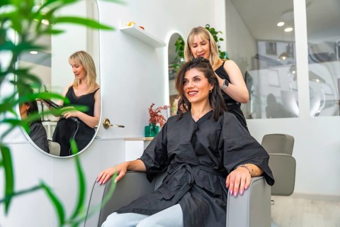 Hairdresser styling hair of smiling customer sitting in armchair in a modern and bright beauty