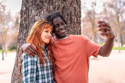 Interracial couple taking a selfie with a smartphone in a park, smiling and enjoying a moment