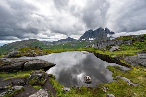 Small lake in mountain landscape, hike to Barden mountain, Breidtind mountain peak behind, Senja,
