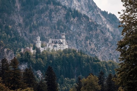 The awe-inspiring Neuschwanstein Castle is situated on rocky, wooded terrain against a dramatic