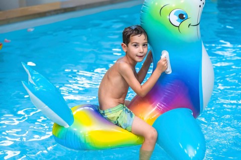 Smiling boy riding a colorful inflatable sea lion toy while splashing in the swimming pool during a