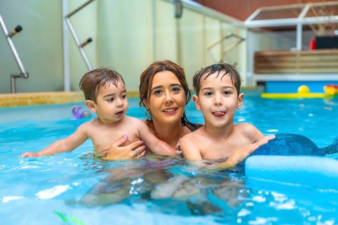 Happy mother embracing her two children while playing and smiling in a swimming pool during summer