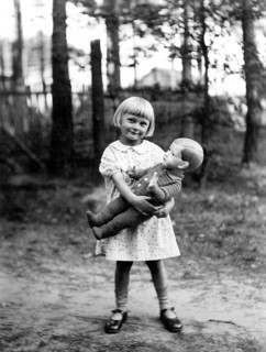 Girl with doll, 1930, Cheerful girl holding a doll in a wooded area on a sunny day, Historical