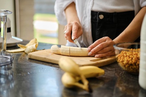 In a warm kitchen, a person slices ripe bananas on a wooden cutting board. Fresh sea buckthorn