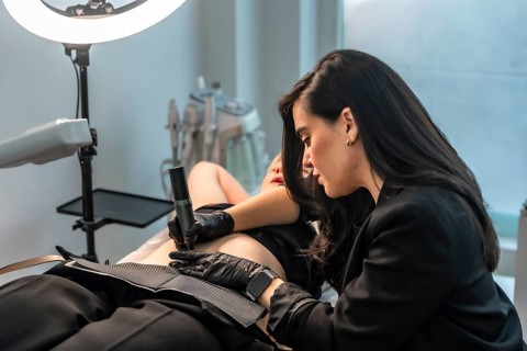 Beautician using a microneedling device, providing a cosmetic treatment to a client lying on a bed