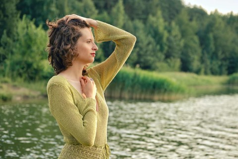 On a hot summer day, a woman stands by the tranquil lake, her hand resting on her head while she