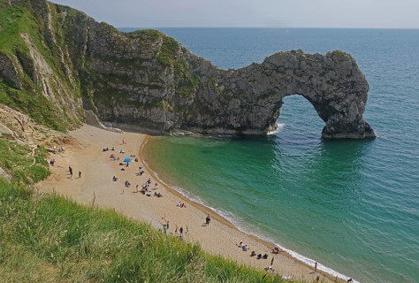 People relaxing on the beach in front of a striking arched cliff and blue sea, Durdle Door,