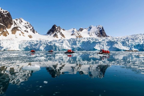 Group of Zodiacs in front of glacier and mountain range with snow, sea, Fugelfjorden, Spitsbergen,