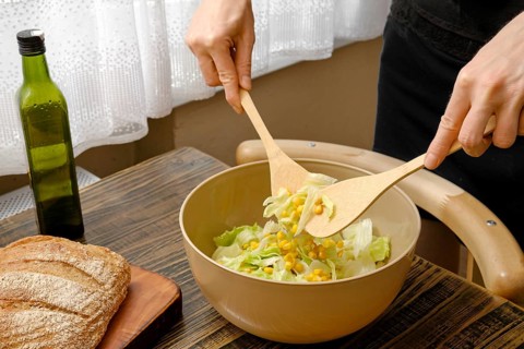 A person stirs a vibrant salad with wooden spoons in a warm and inviting kitchen. Fresh lettuce and