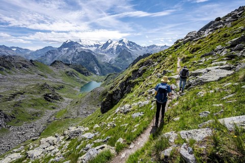 Mountaineer on hiking trail in mountain landscape, descent at Col du Louvie, view of mountain lake